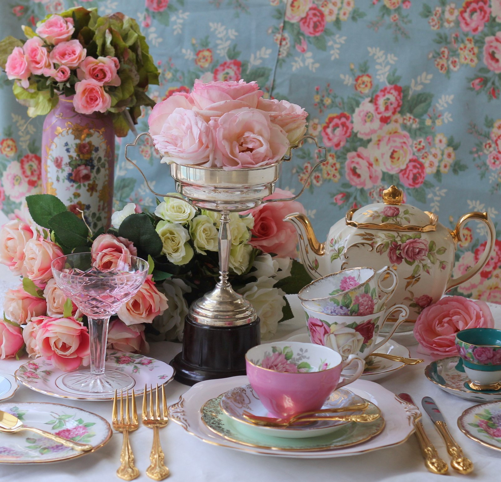 Vintage floral teacups, silverware and roses arranged for a high tea